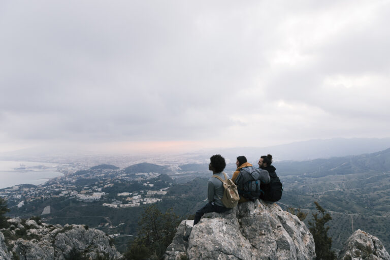 three-friends-sitting-top-mountain-enjoying-scenic-view