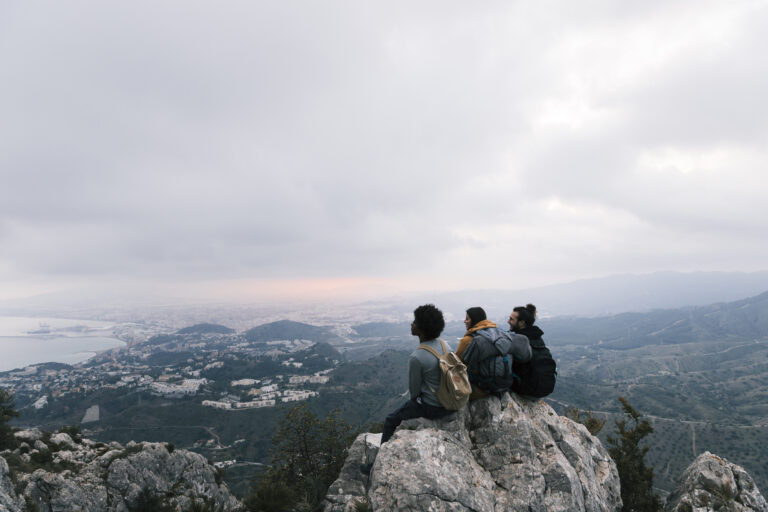 three friends sitting top mountain enjoying scenic view