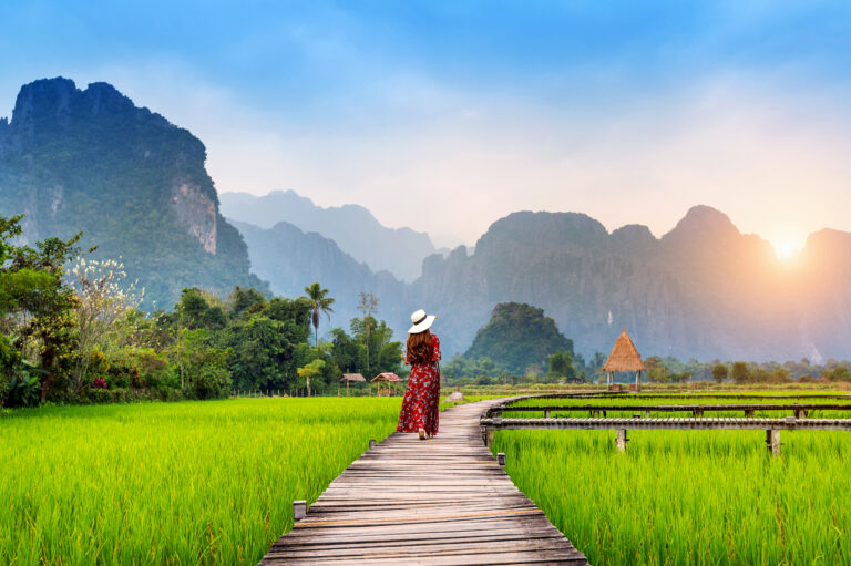 Young woman walking on wooden path with green rice field in Vang Vieng, Laos.